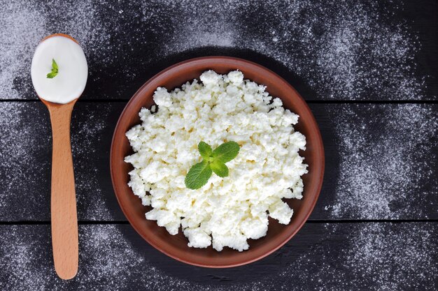 Cottage cheese in clay bowl on wooden boards Sour cream in wooden spoon Dairy products on dark background