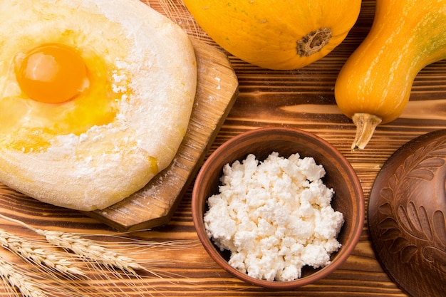 Cottage cheese in an earthenware bowl next to dough and pumpkins. rustic