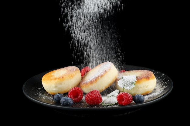 Cottage cheese fritters in a plate with berries Powdered sugar is sprinkled