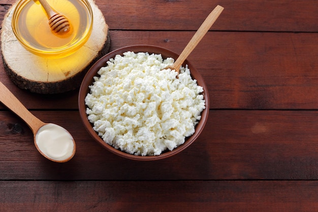 Cottage cheese and honey on wooden boards Cottage cheese in clay plate and cream in wooden spoon Top view