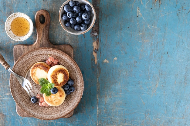 Cottage cheese pancakes cheesecakes ricotta fritters with fresh blueberries currants and peaches on a plate Healthy and delicious breakfast for the holiday Blue wooden background