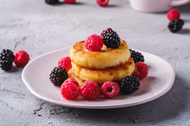 Cottage cheese pancakes, curd fritters dessert with raspberry and blackberry berries in plate on stone concrete table, angle view macro