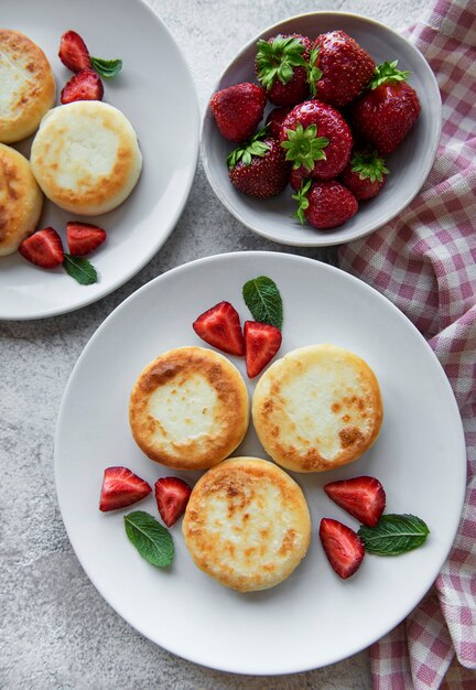 Cottage cheese pancakes, ricotta fritters on ceramic plate with  fresh strawberry. Healthy and delicious morning breakfast.  Grey concrete background.