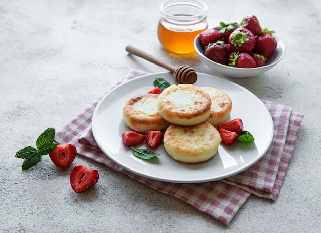 Cottage cheese pancakes, ricotta fritters on ceramic plate with  fresh strawberry. Healthy and delicious morning breakfast.  Grey concrete background.