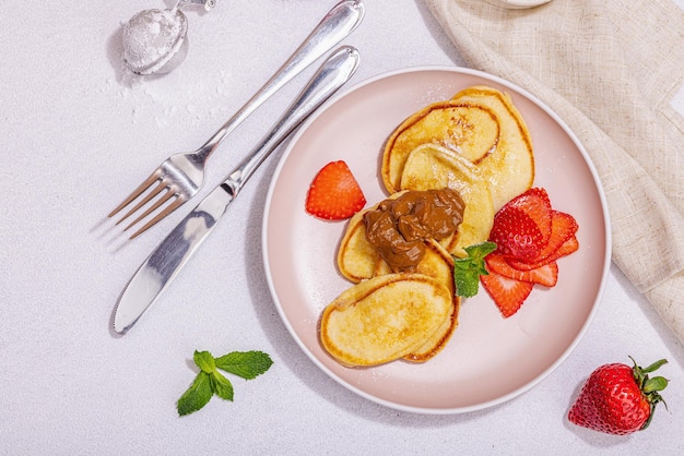 Cottage cheese pancakes syrniki curd fritters with strawberry mint and powdered sugar on a pink plate Selective focus delicious breakfast Trendy stone concrete background top view