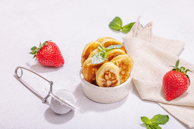 Cottage cheese pancakes syrniki curd fritters with strawberry mint and powdered sugar in a portion bowl Selective focus delicious breakfast Trendy stone concrete background copy space