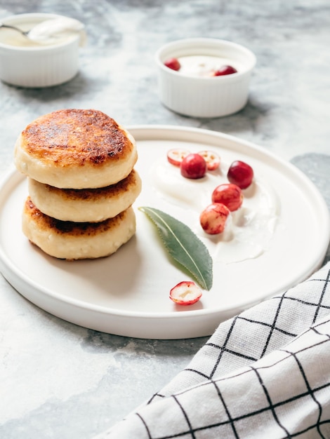 Cottage cheese pancakes on a table with sour cream and berries Delicious and healthy cheesecakes with cranberry for breakfast Yummy dessert Vertical view soft focus