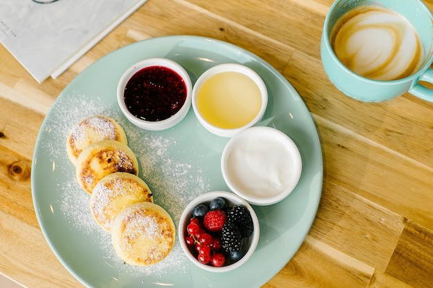 Cottage cheese pancakes with fresh berries and cappuccino coffee on wooden table Top view