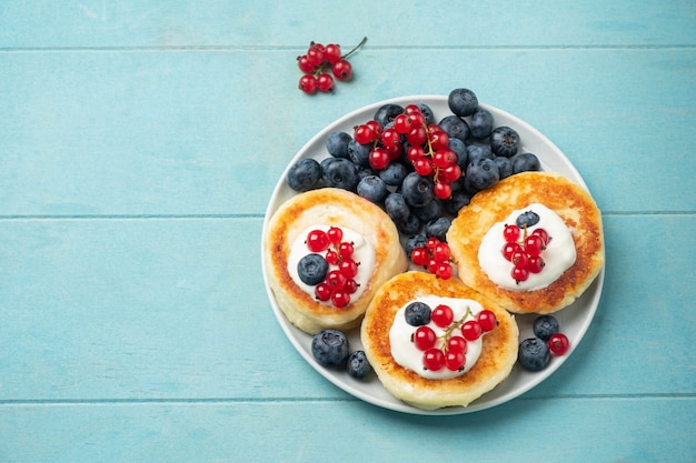 Cottage cheese pancakes with red currant and blueberry on blue table