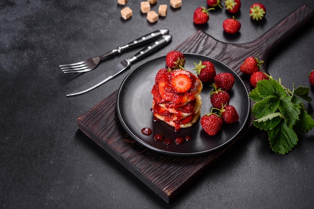 Cottage cheese pancakes with sliced strawberries and strawberry jam on a plate on a concrete background