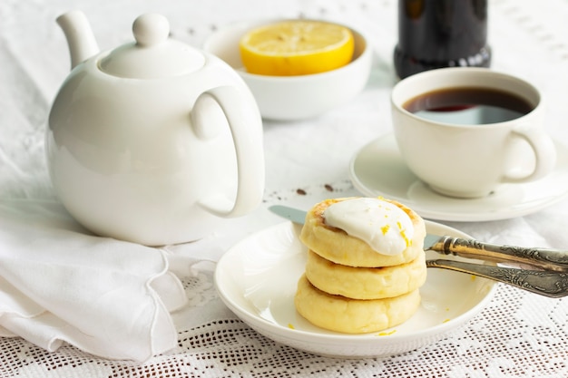 Cottage cheese pancakes with sour cream and lemon zest, served with tea. Selective focus.