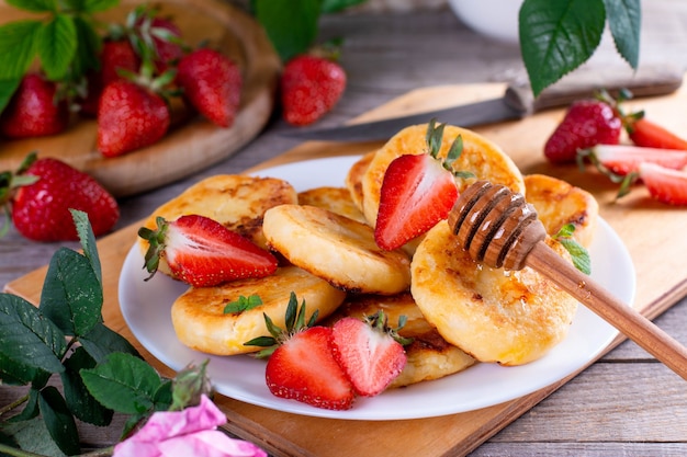 Cottage cheese pancakes with strawberry on a white plate on a wooden table. Breakfast or Lunch Concept.