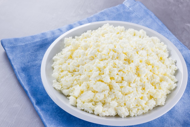 Cottage cheese in a plate. Fresh cottage cheese in white plate . Soft cheese on a blue napkin