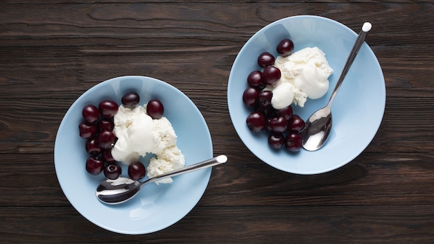 Cottage cheese with delicate sour cream and ripe sweet cherries in blue bowls on a wooden table