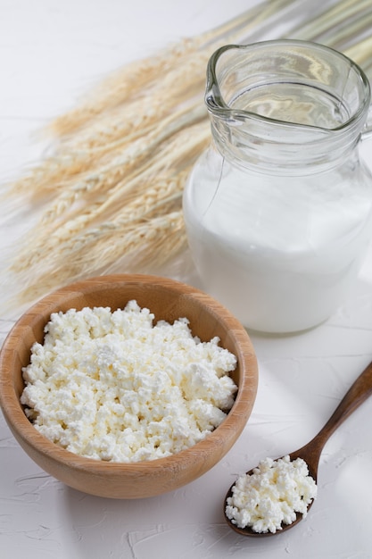 Cottage cheese  with milk and wooden spoon on white background.