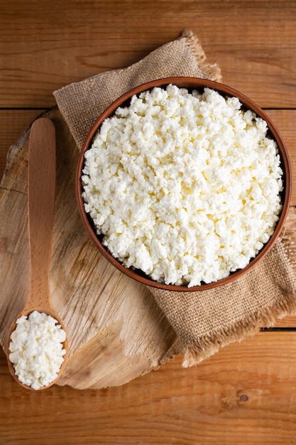 Cottage cheese on a wooden stand Fresh cottage cheese in a bowl Soft cheese and wooden spoon