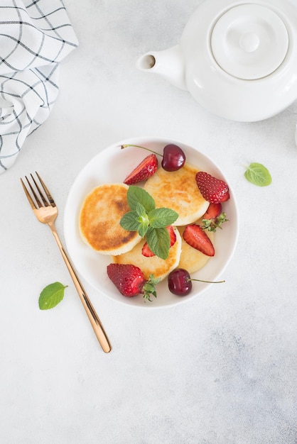 Cottage cheesecakes with berries and mint in a white plate on a white background Top view