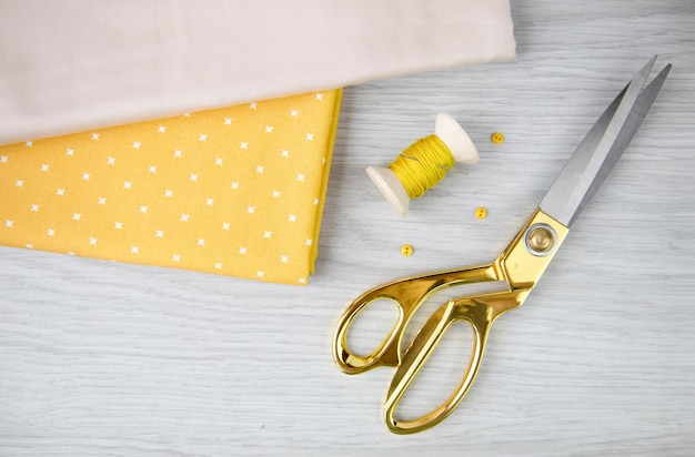 cotton fabric scissors and a spool of yellow thread on a light wooden table