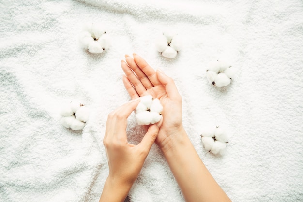 Cotton flowers in a female elegant hand with manicure on a wallof a white terry towel