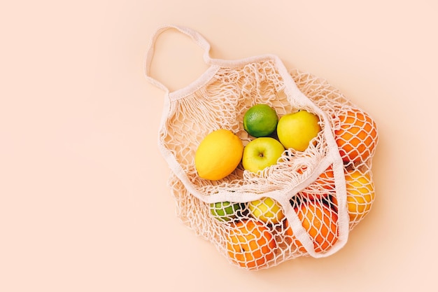 Cotton mesh bag with fresh colorful fruits on beige background, top view. Zero waste concept