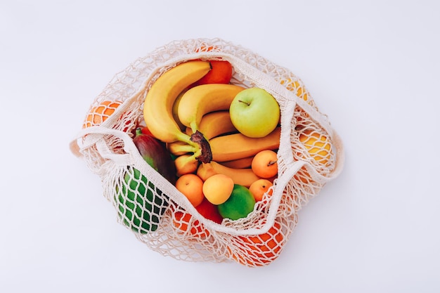 Cotton mesh bag with fresh colorful fruits on light background, top view. Zero waste concept