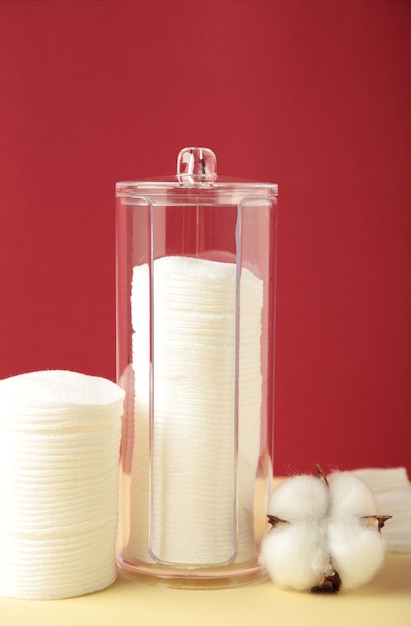 Cotton pads in containers with cotton flower on beige and red background Vertical photo