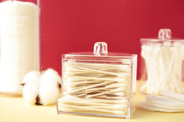 Cotton pads and cotton sticks in containers with cotton flower on red background