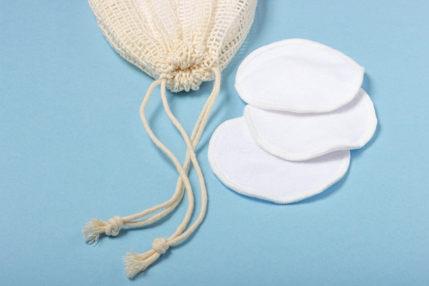 Cotton reusable make-up remover pads in a cloth bag and face wash and cleanser on a blue background. The concept of ecology and conscious consumption. Reusable cotton pads