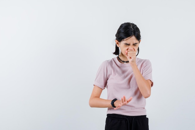 Coughing teenage girl covers her mouth with her fist on white background