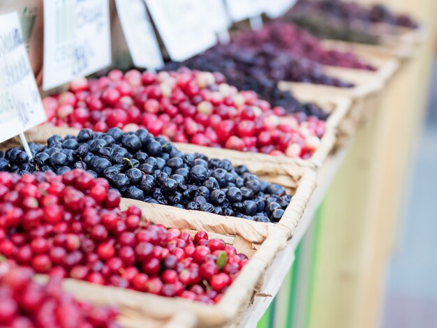 Counter in the market with a variety of ripe berries in wicker trays. Summer season.