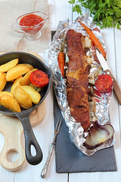 Country dinner - roasted veal chops with vegetables and potatoes on a white wooden table