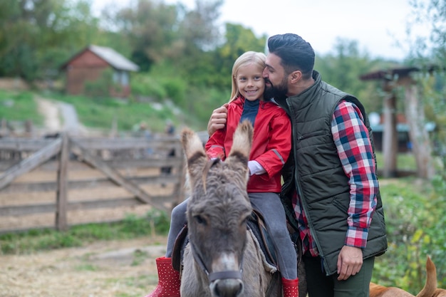 Country life. Father and daughter at the cattle-farm with a donkey