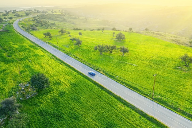 Countryside green landscape with a car driving down an asphalt road and a car view from above