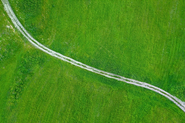 Countryside road across field of green grass aerial view directly above