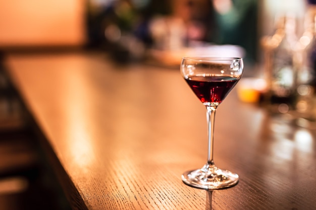 A coupe glass with red port wine at the bar counter. A horizontal lifestyle photo with shallow depth of field and copy space.