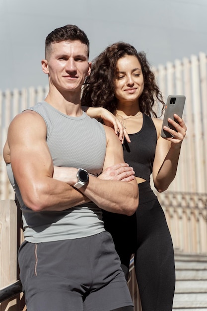 Couple of athletes resting after hard street workout session embracing using smartphone