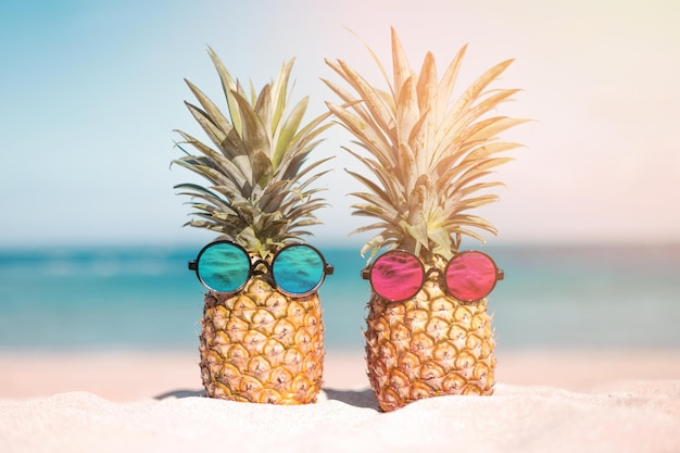 Couple of attractive pineapples in stylish mirrored sunglasses on the sand against turquoise sea