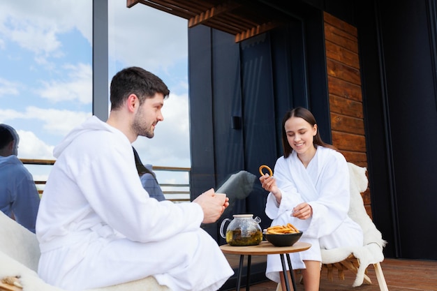 Couple in bathrobes drinking tea with bagels after spa treatments