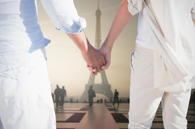 Couple on the beach looking out to sea holding hands against eiffel tower