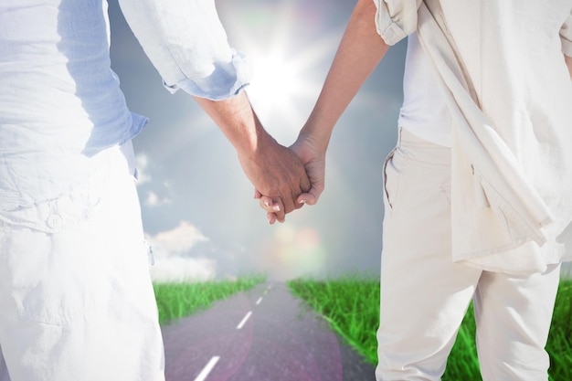 Couple on the beach looking out to sea holding hands against road on grass