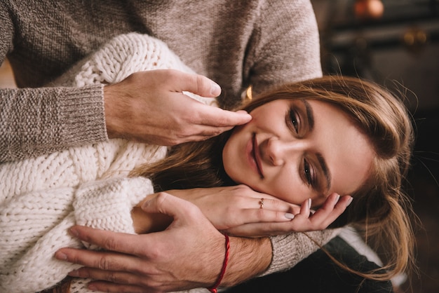 Couple on the bed in the bedroom. Dark interior. Hugs and kisses. Be in love. White sweater and high socks. Romantic meeting. A date lovers. Tenderness. The guy strokes the girl on the cheek.