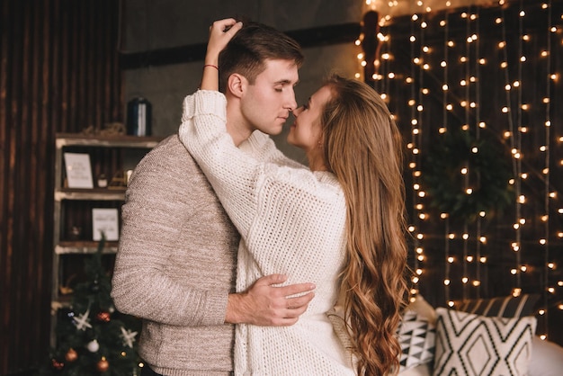 Couple on the bed in the bedroom. Dark interior. New Year's and Christmas. Hugs and kisses. Love. White sweater and high socks. Romantic meeting. A date lovers.