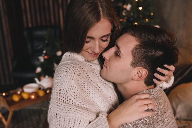 Couple on the bed in the bedroom. Dark interior. New Year's and Christmas. Hugs and kisses. Love. White sweater and high socks. Romantic meeting. A date lovers.