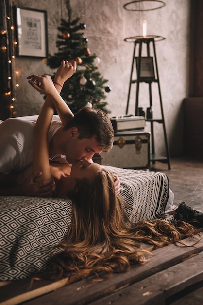 Couple on the bed in the bedroom dark interior new years and christmas hugs and kisses love white sw...