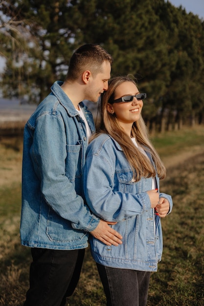 A couple in a blue denim jacket stands in a field and the girl is wearing sunglasses.