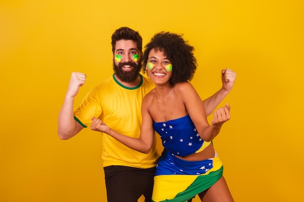 Couple of brazilian soccer fans dressed in the colors of brazil black woman caucasian man screaming yes celebrating victory