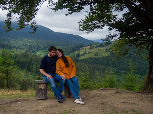 Couple in casual clothes sit under large tree with forest background