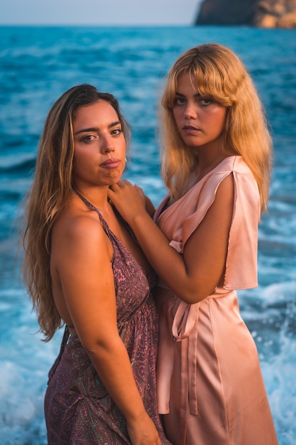 A couple of Caucasian girls in pink dresses, posing summer on the beach by the sea