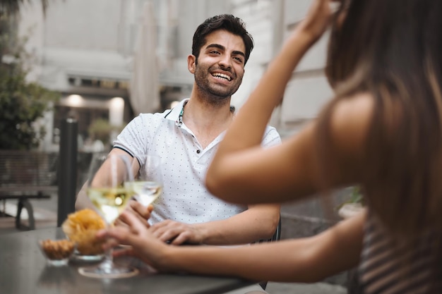 Couple celebrating in outdoor cafe and having a glass of white wine focus on man face unrecognizable woman alcohol dating and lifestyle concept