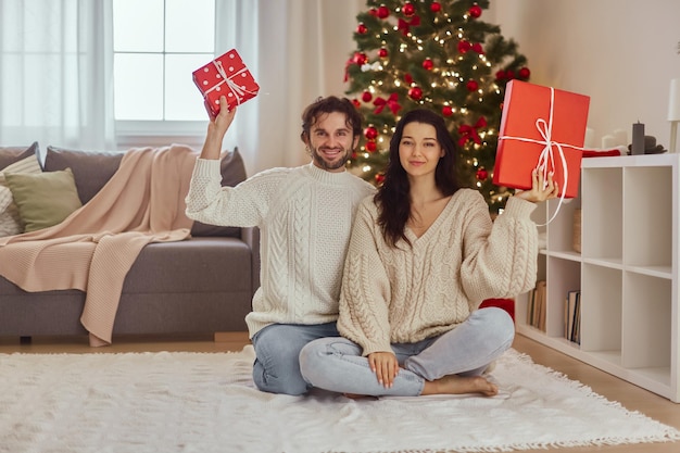 Couple celebration new year near christmas tree at home holding presents in the gift boxes